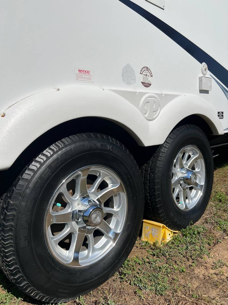 Aluminum wheels and black tires on a tandem-axle RV trailer, beside a clean white fender