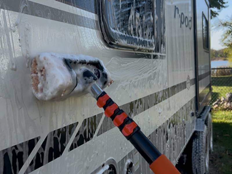 Wash brush on an extension pole scrubbing soap across the sidewall of a travel trailer