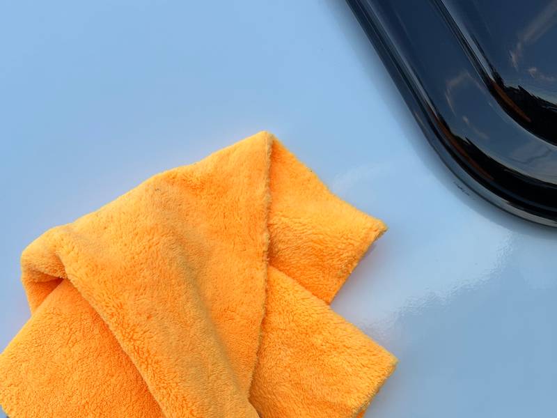 Orange microfiber towel buffing the glossy white front cap of a travel trailer